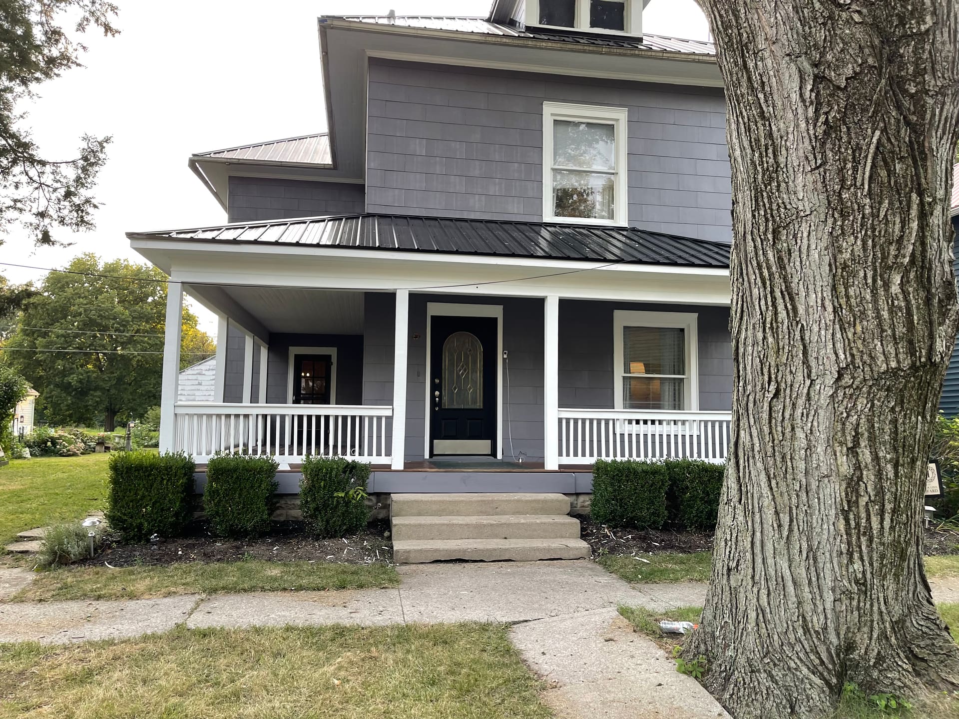 Front view of a two-story gray-painted home with white porch and brick chimney