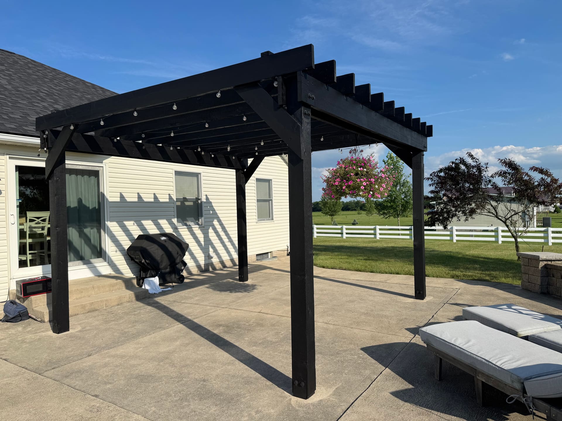 Black wood pergola over a concrete patio with bistro lights overhead