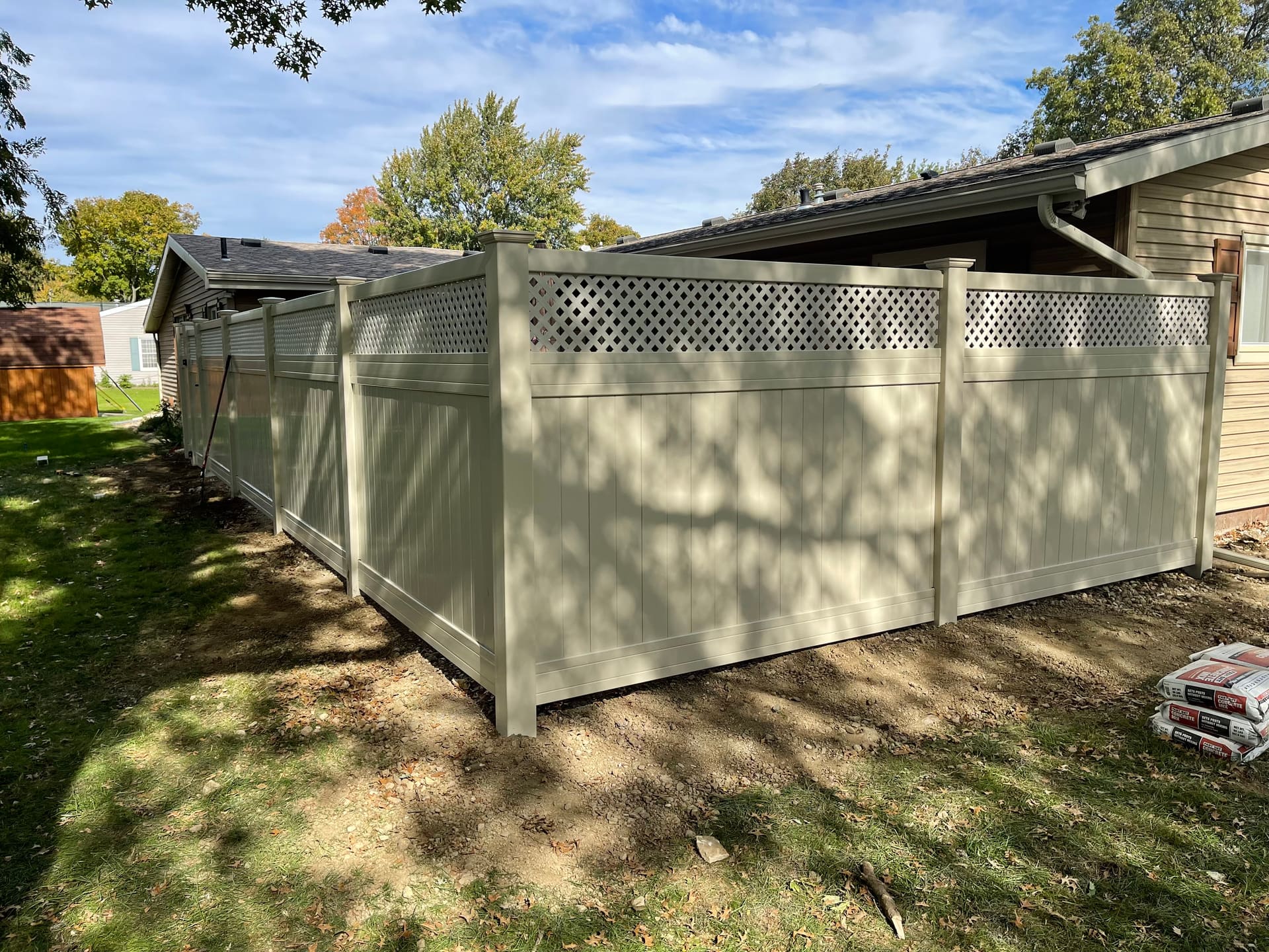 Tan vinyl privacy fence with lattice top installed alongside a single-story home