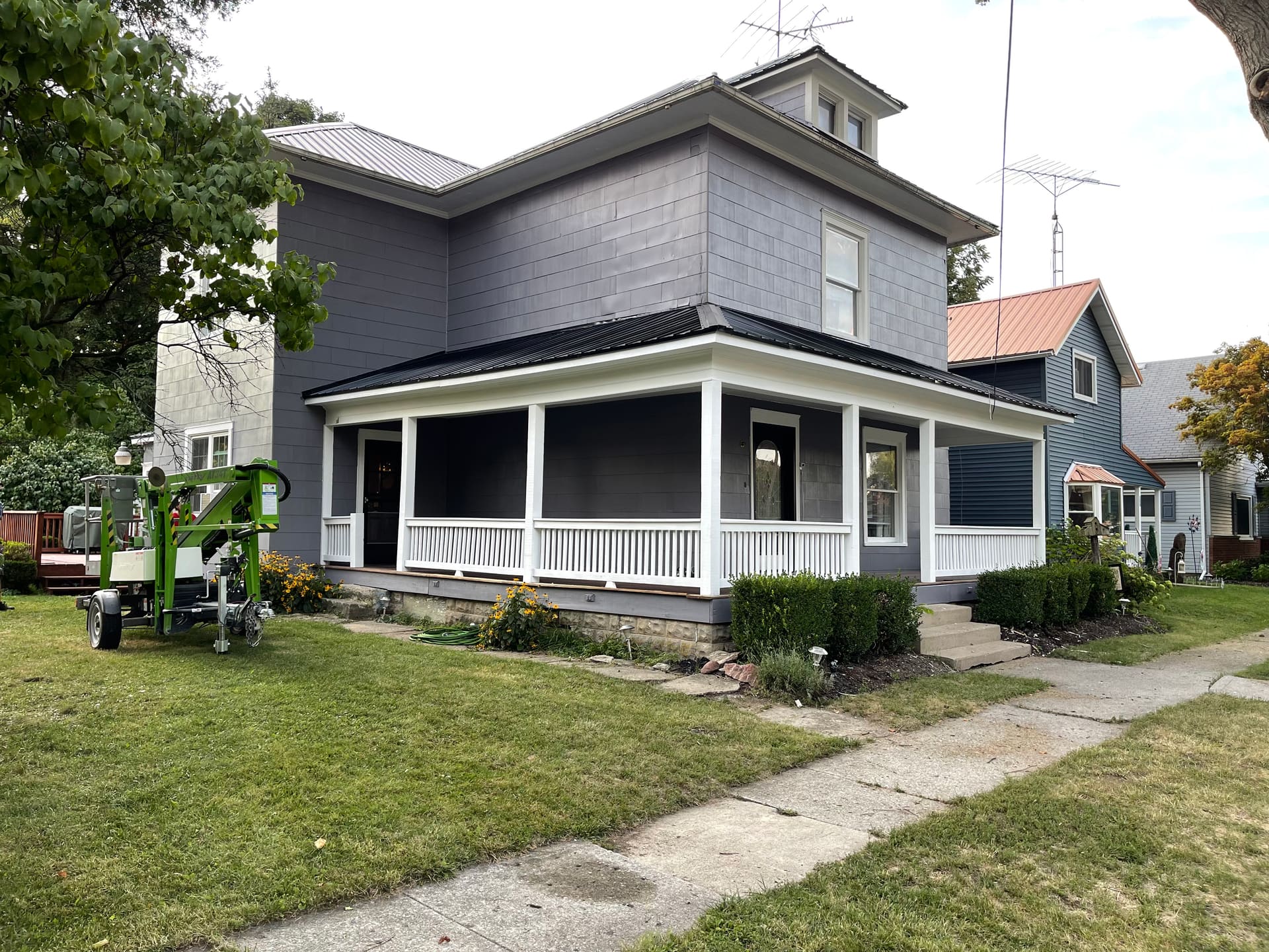 Two-story gray exterior repaint, side angle with the painting crew's lift on site